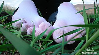 Feet in Cute White Socks with Jeans on the Grass Field